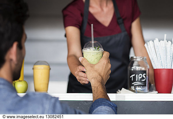 Midsection of female owner giving smoothie to customer at food truck