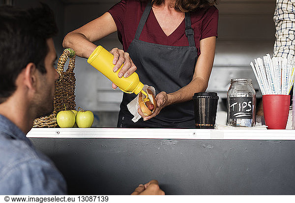 Midsection of female vendor serving hotdog for customer at food truck