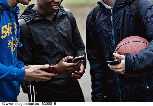 Midsection of friends holding smart phones while standing on basketball court