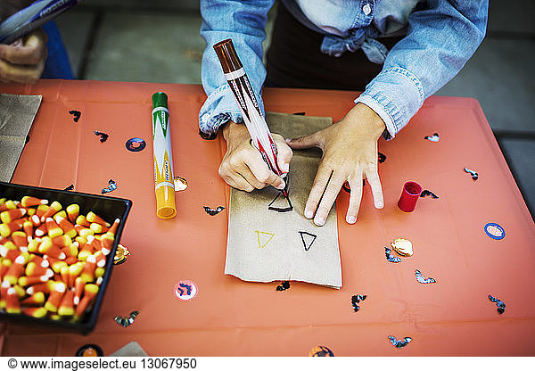 Midsection of girl decorating paper bag at table during Halloween party