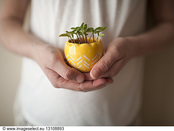 Midsection of girl holding potted plant while standing by wall at home