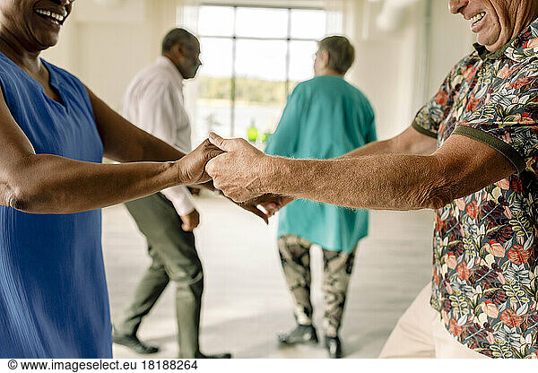 Midsection of happy senior couple holding hands while practicing dance in class
