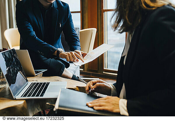 Midsection of male and female colleagues discussing over document in office