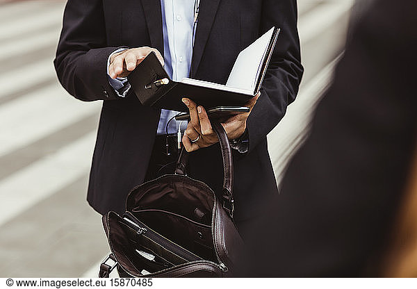 Midsection of male business person holding book while standing outdoors