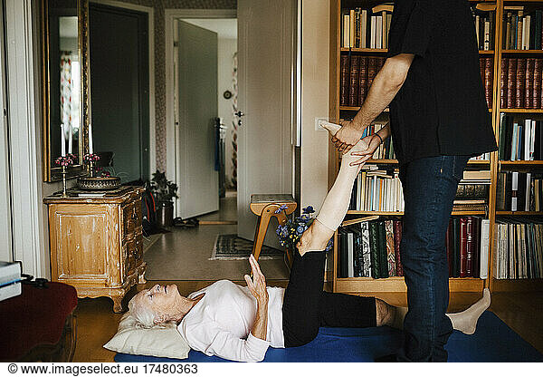 Midsection of male caregiver guiding senior woman while exercising at home