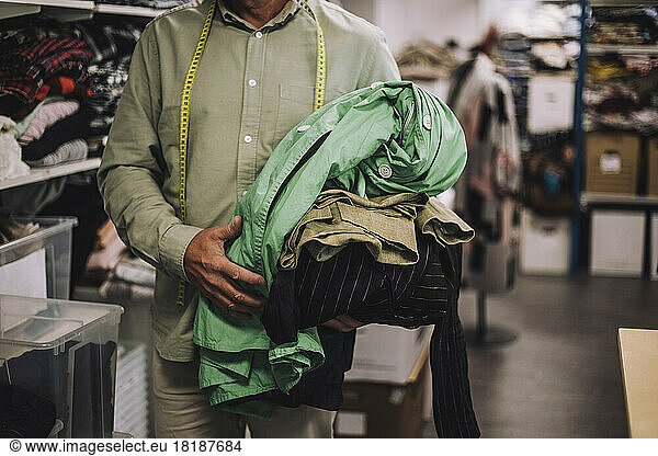 Midsection of male fashion designer holding clothes at workshop
