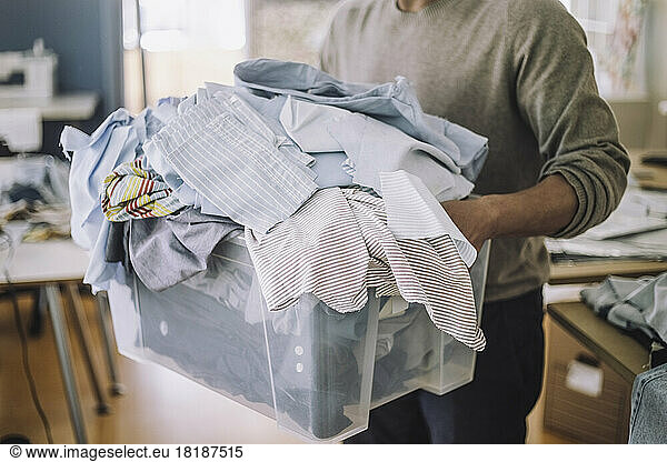 Midsection of male fashion designer holding recycled clothes in container