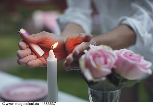 Midsection of man covering lit candle on table at garden party