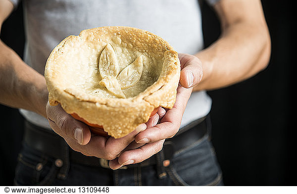 Midsection of man holding chicken pot pie against black background