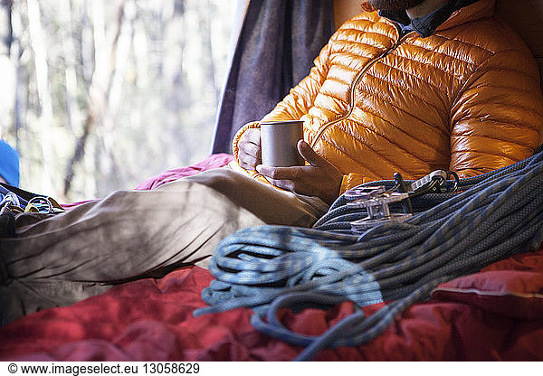 Midsection of man holding mug while sitting on bed in camper van
