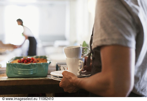 Midsection of man holding plates and coffee cups at cafe