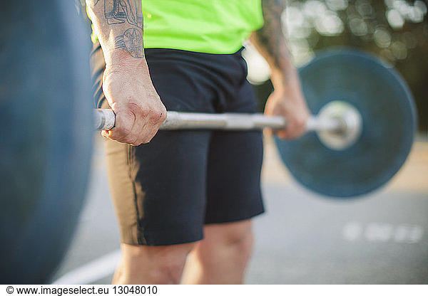 Midsection of man lifting barbell at park