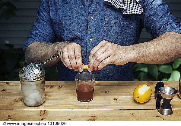 Midsection of man squeezing lemon in alcohol glass at table