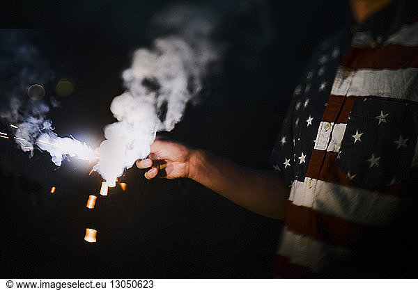 Midsection of man wearing American Flag t-shirt while holding sparkler during night
