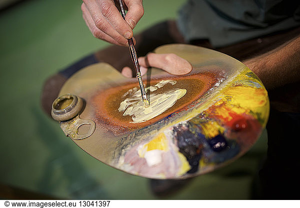 Midsection of man with watercolor paint palette in workshop
