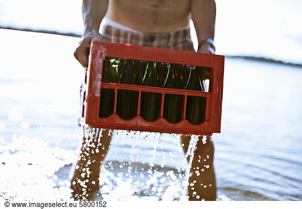 Midsection of mature man carrying drinks crate in lake water
