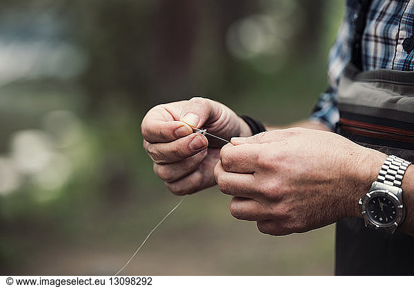 Midsection of mature man holding fishing thread outdoors