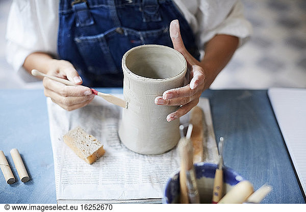 Midsection of mature woman learning pottery at table in art class