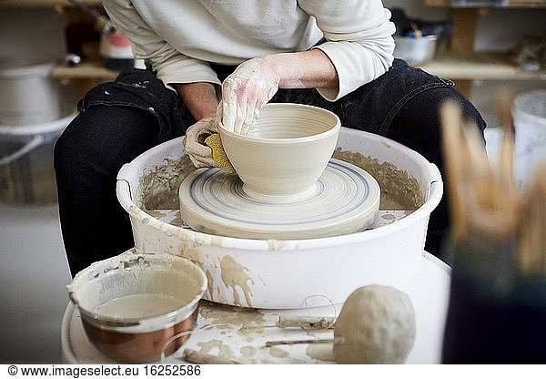 Midsection of mid adult woman molding pot in pottery class