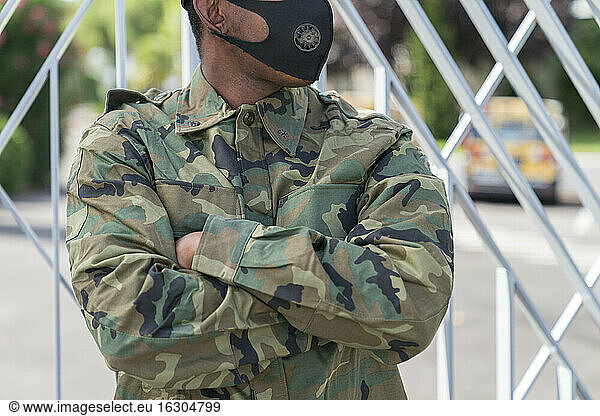 Midsection of military soldier with arms crossed standing against gate