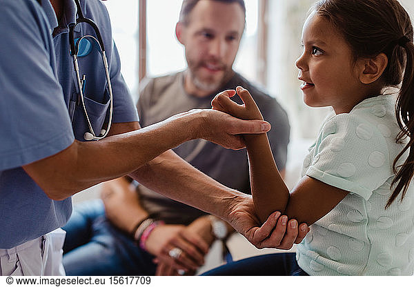 Midsection of nurse examining girl sitting with father at clinic