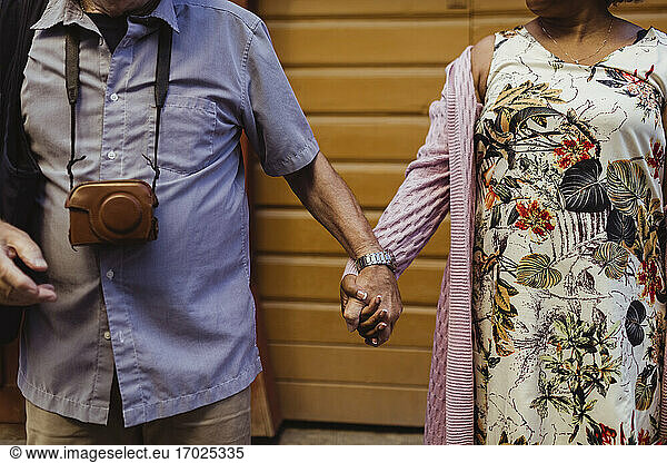 Midsection of senior couple holding hands against wall
