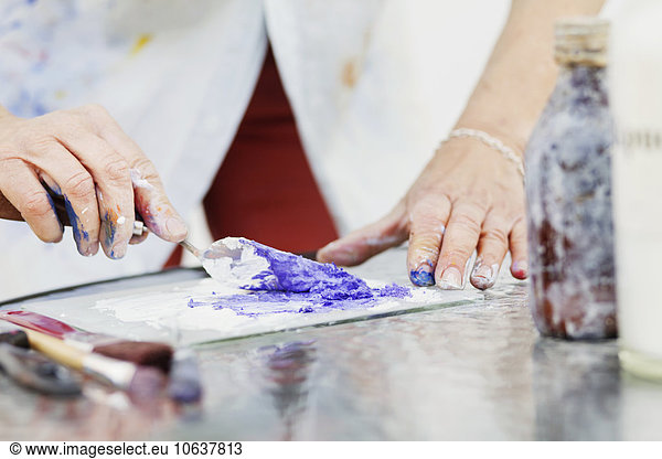 Midsection of senior female artist mixing paint in studio