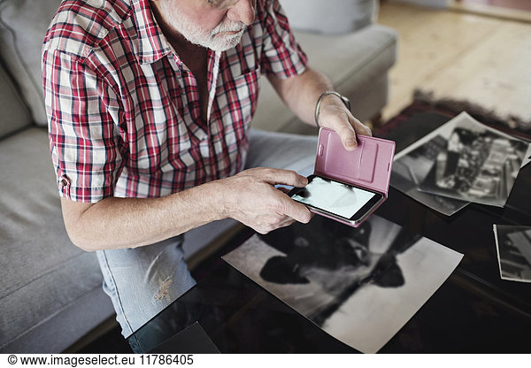 Midsection of senior man photographing old photograph through smart phone at home