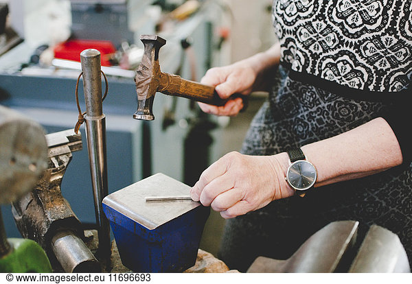 Midsection of senior woman hammering on metal to make jewelry in workshop