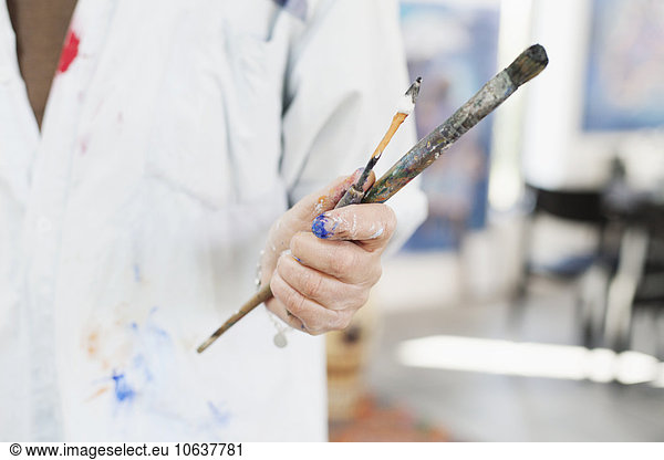 Midsection of senior woman holding paintbrush and painting knife