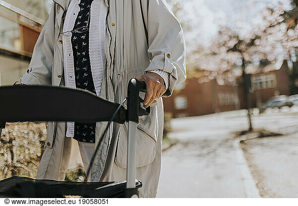 Midsection of senior woman with walker on sidewalk