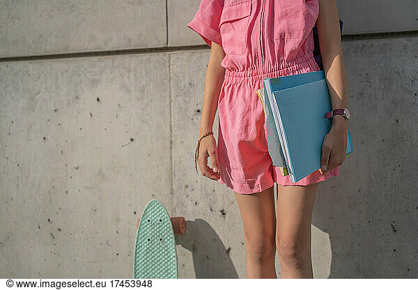 Midsection of teenage girl with skateboard and hotebooks
