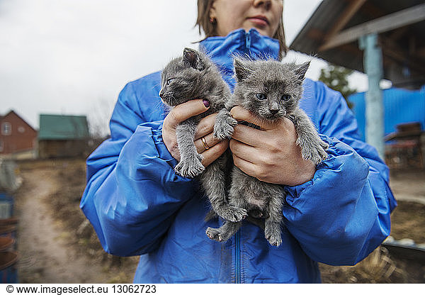 Midsection of woman carrying kittens while standing on field