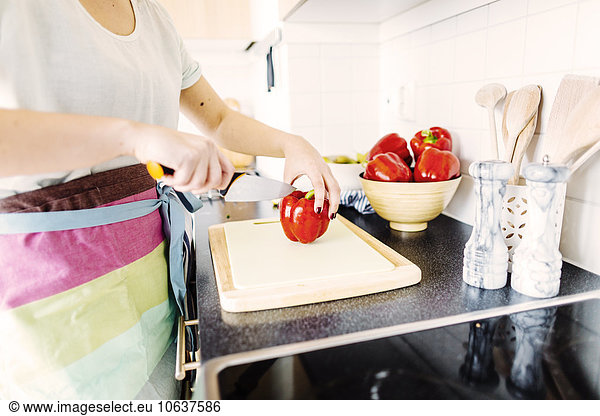 Midsection of woman cutting red bell pepper at kitchen counter