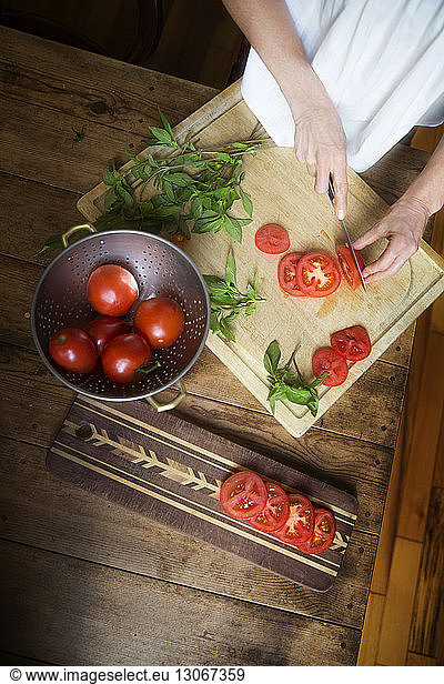 Midsection of woman cutting tomato slices by mint leaves on cutting board