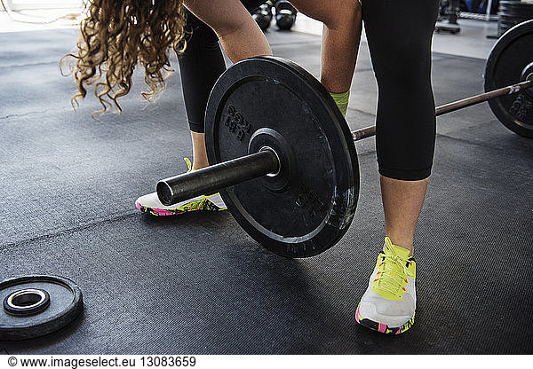 Midsection of woman exercising with barbell at crossfit gym