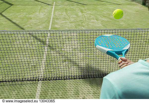 Midsection of woman hitting tennis ball with racket on court