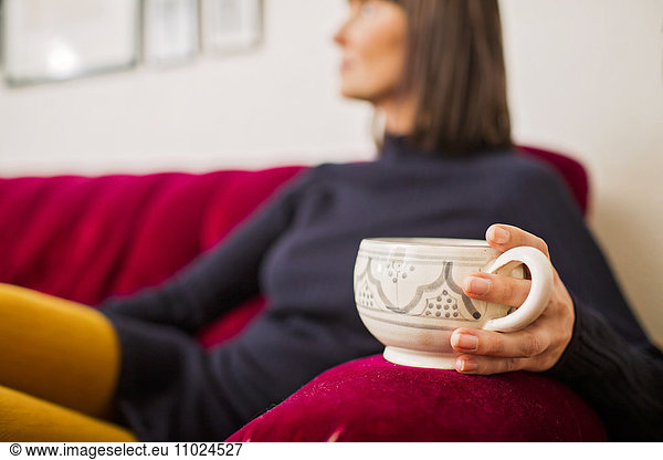 Midsection of woman holding coffee cup while resting on sofa