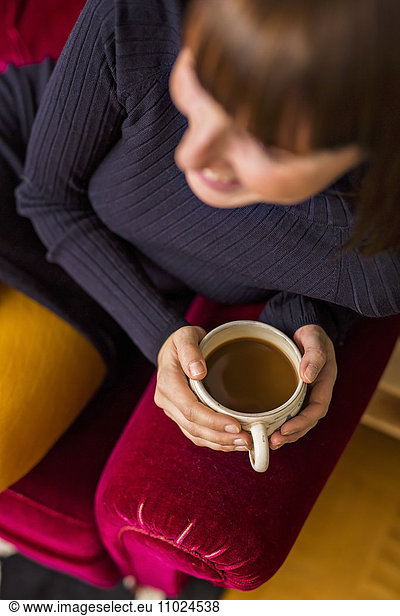 Midsection of woman holding coffee cup while sitting on sofa