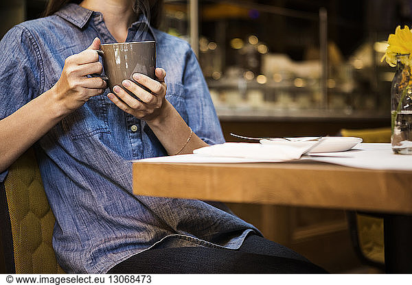 Midsection of woman holding coffee mug sitting at table in cafe