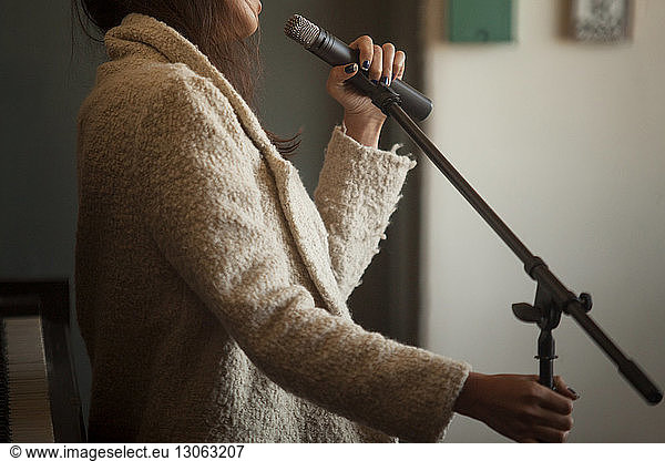 Midsection of woman holding microphone while standing at home