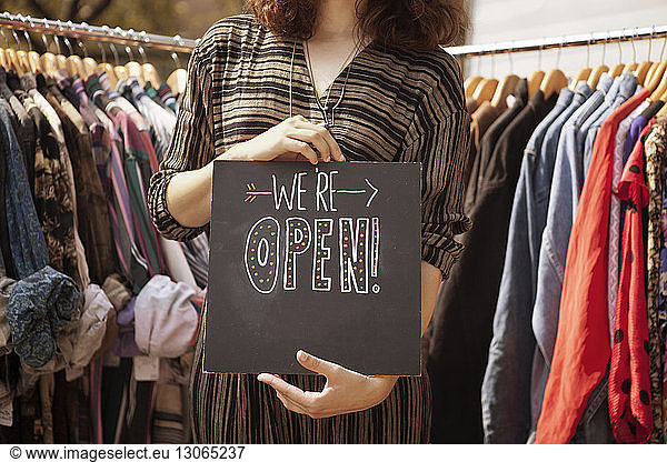 Midsection of woman holding opening board while standing by clothes racks