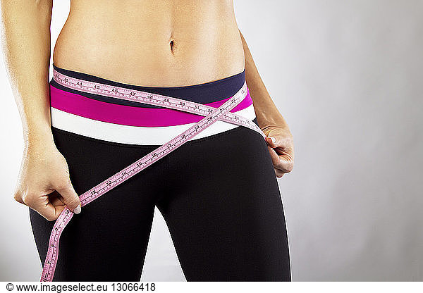 Midsection of woman measuring waist against gray background