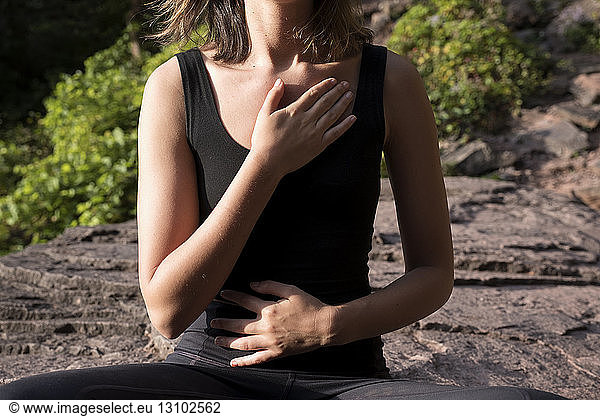 Midsection of woman mediating while touching chest and abdomen during sunny day