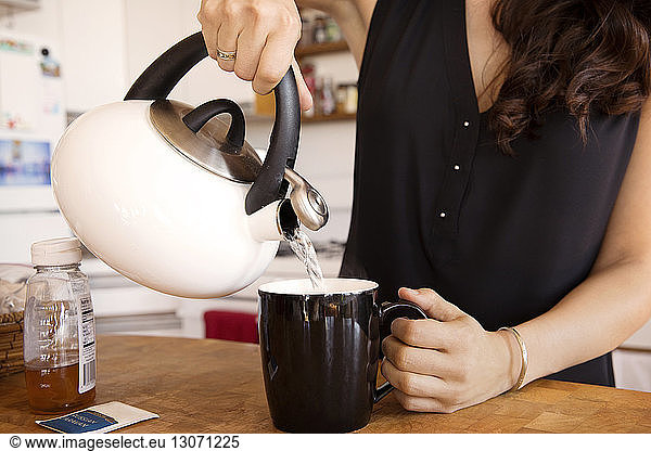 Midsection of woman pouring water in mug at kitchen counter