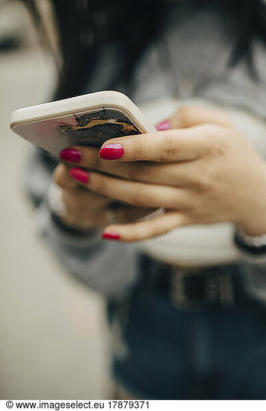 Midsection of woman text messaging through smart phone