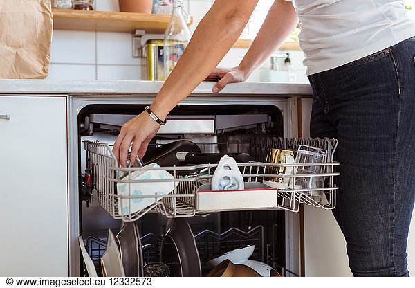 Midsection of woman using dishwasher while standing in kitchen