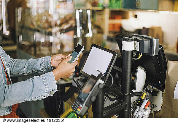 Midsection of woman using smart phone while scanning QR code for payment at store checkout