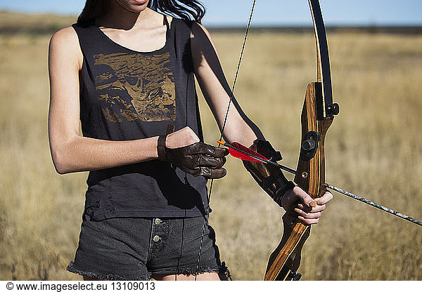 Midsection of woman with bow and arrow on field