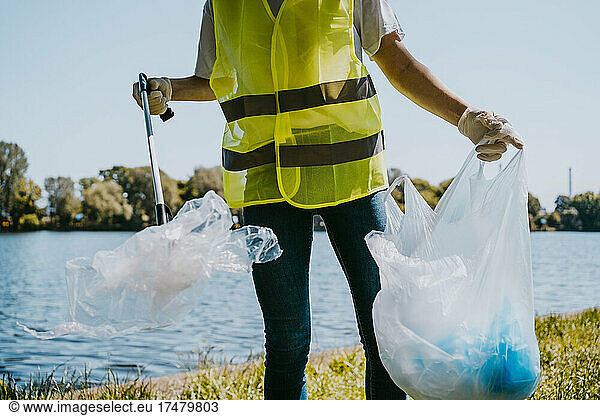 Midsection of young male environmentalist picking up plastic against lake